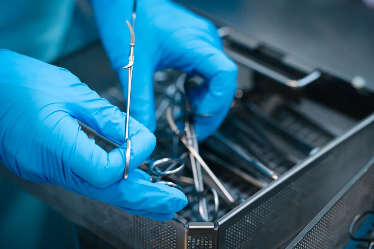 Behandschuhte Hände prüfen ein chirurgisches Instrument im Sieb